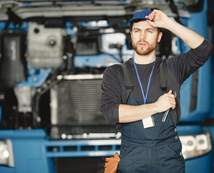 Worker in uniform. Man repairs a truck. Man with tools